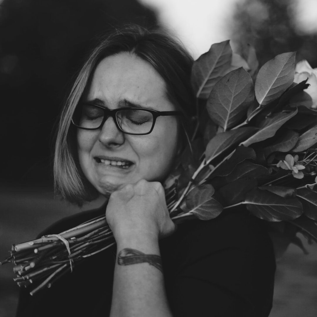 grayscale photo of crying woman holding bouquet of flowers